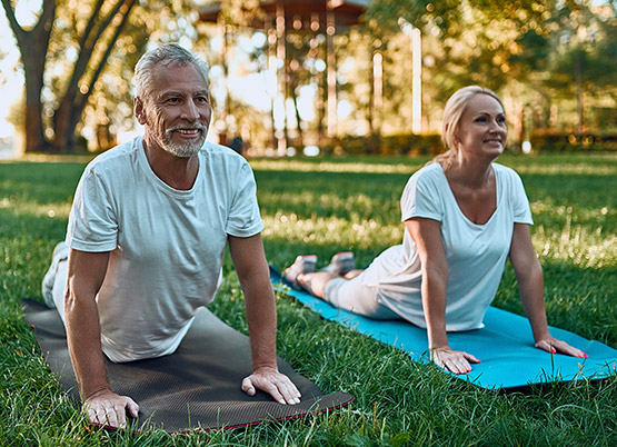 an elderly couple on yoga mats outside stretching their backs 