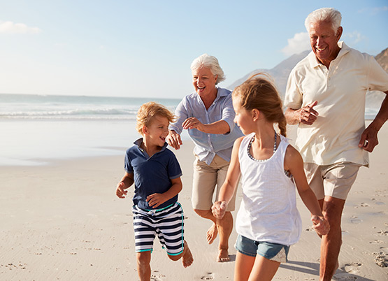 family of grandparents and children running along beach  