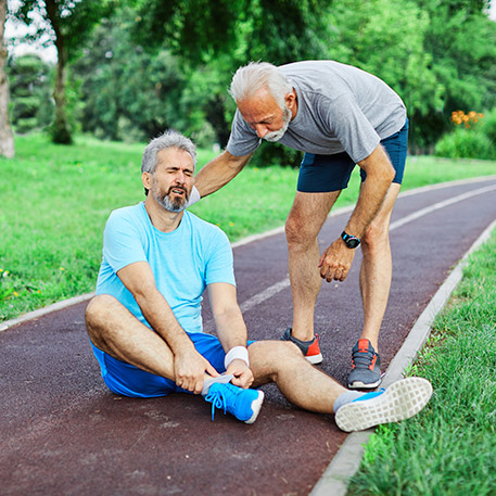 Man sitting on running track with injured foot with another male comforting him