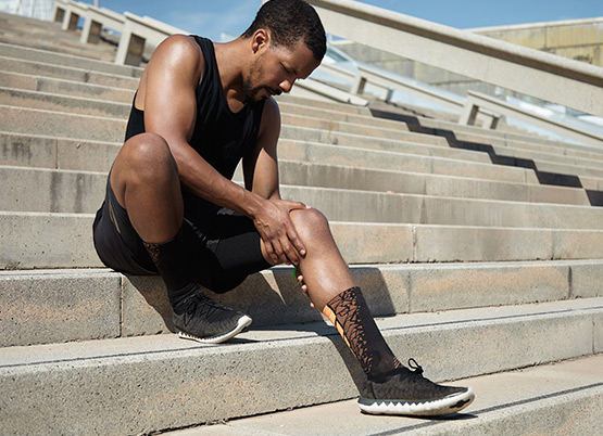 A man sitting on some steps with knee pain during exercise
