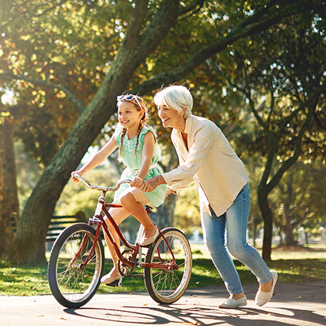 granny teaches granddaughter to ride bike in park 