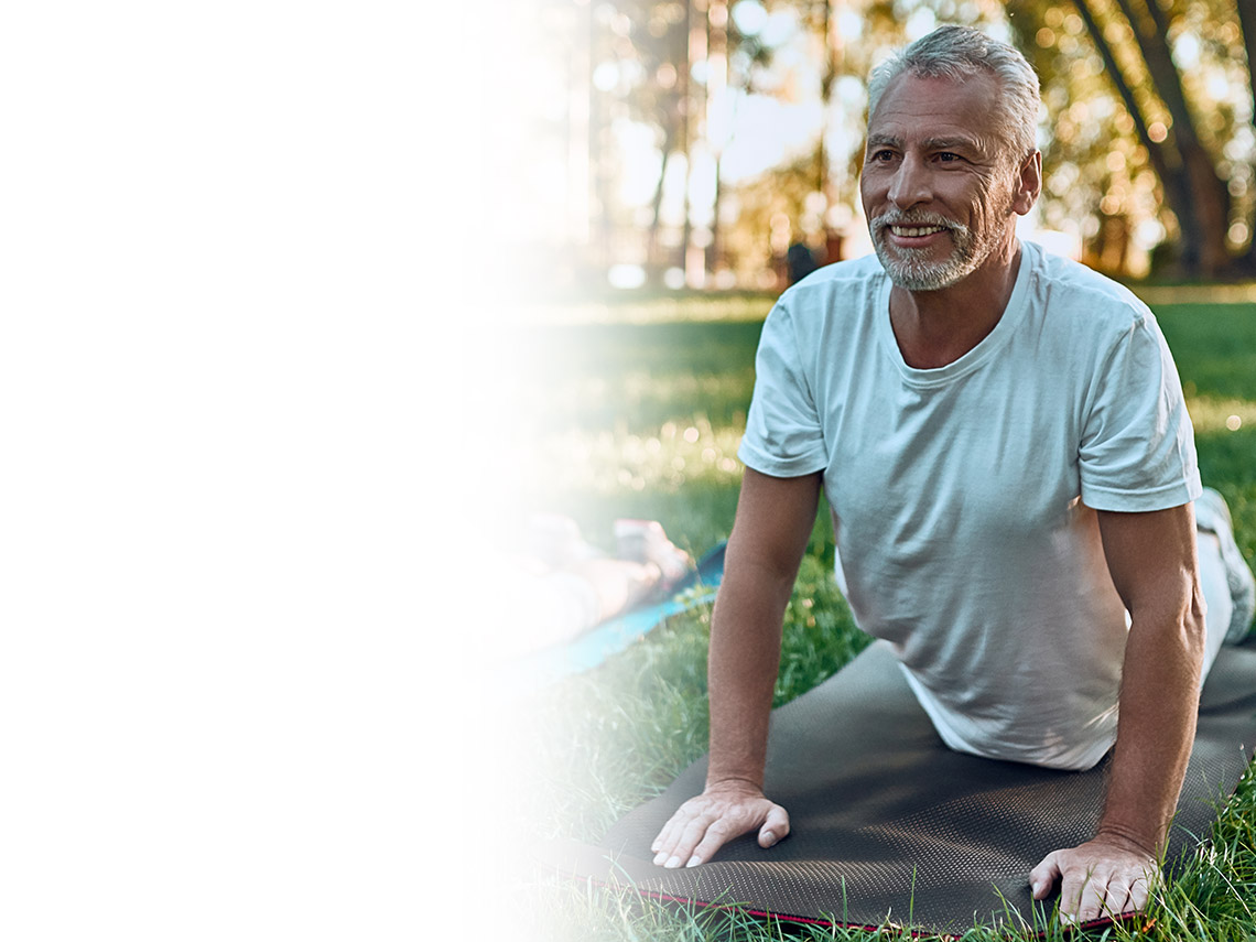 an elderly couple on yoga mats outside stretching their backs